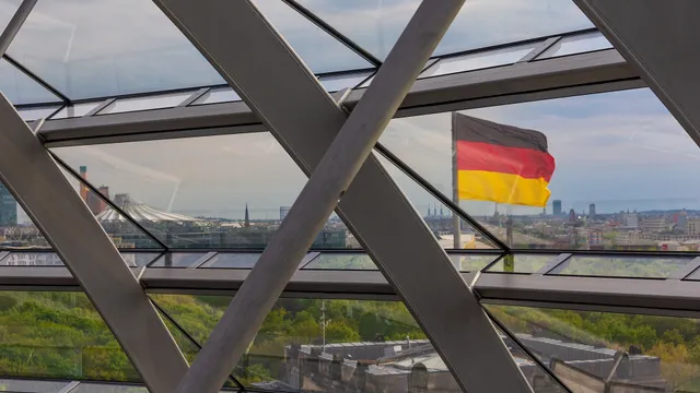 Die deutsche Flagge über Berlin, gesehen durch die Glas-Stahl-Konstruktion der Reichstagskuppel, als Rahmen für eine Studie zur Abhängigkeit deutscher KI-Unternehmen von Modellanbietern.