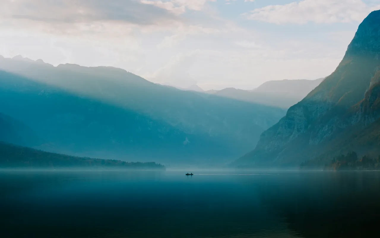 A still lake between misty mountains at dawn, with a small boat in the distance.